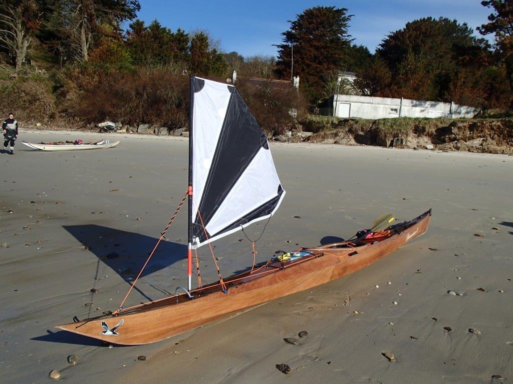 Didier a équipé le Shearwater 17 qu'il a construit l'été dernier d'un gréement de portant. Lorsqu'il n'est pas utilisé, le mât est replié en arrière et la voile est pliée en éventail. On dresse le gréement en tirant sur l'étai, renvoyé sur un coinceur à l'avant du cockpit. Simple, pratique et élégant. Didier écrit : "Ce système de voile fonctionne super bien. Dimanche dernier par vent de force 6, le kayak surfait de vague en vague, à peine besoin de pagayer. En jouant avec la dérive on dirige le kayak parfaitement. C'est vraiment un très bon bateau qui démarre au surf très facilement." 