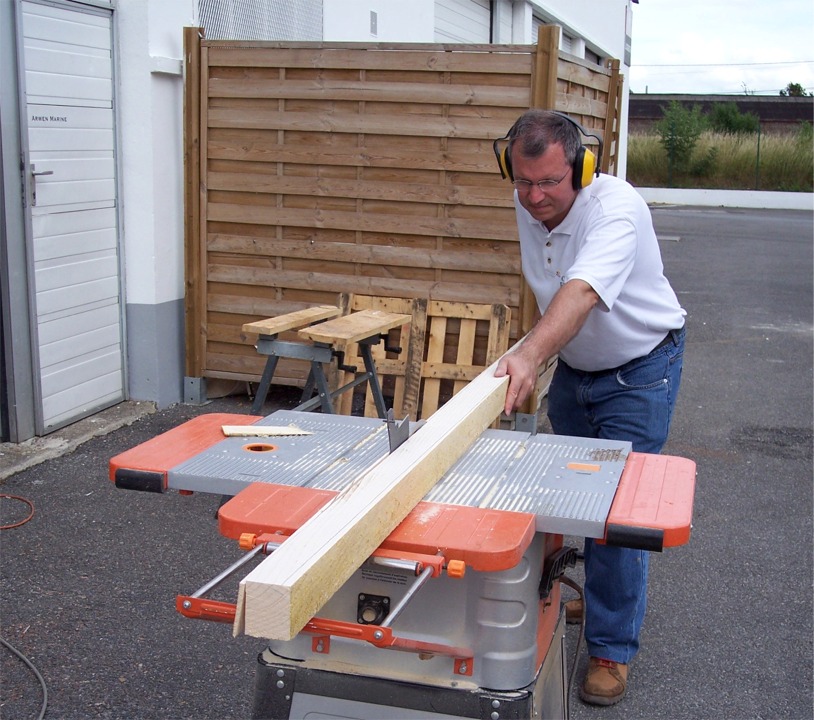 Pendant que l'époxy durcit, nous commençons le travail sur les espars. Sur cette image, Gilles utilise la scie de table pour faire une coupe sur une face du mât afin d'affiner sa partie haute. 