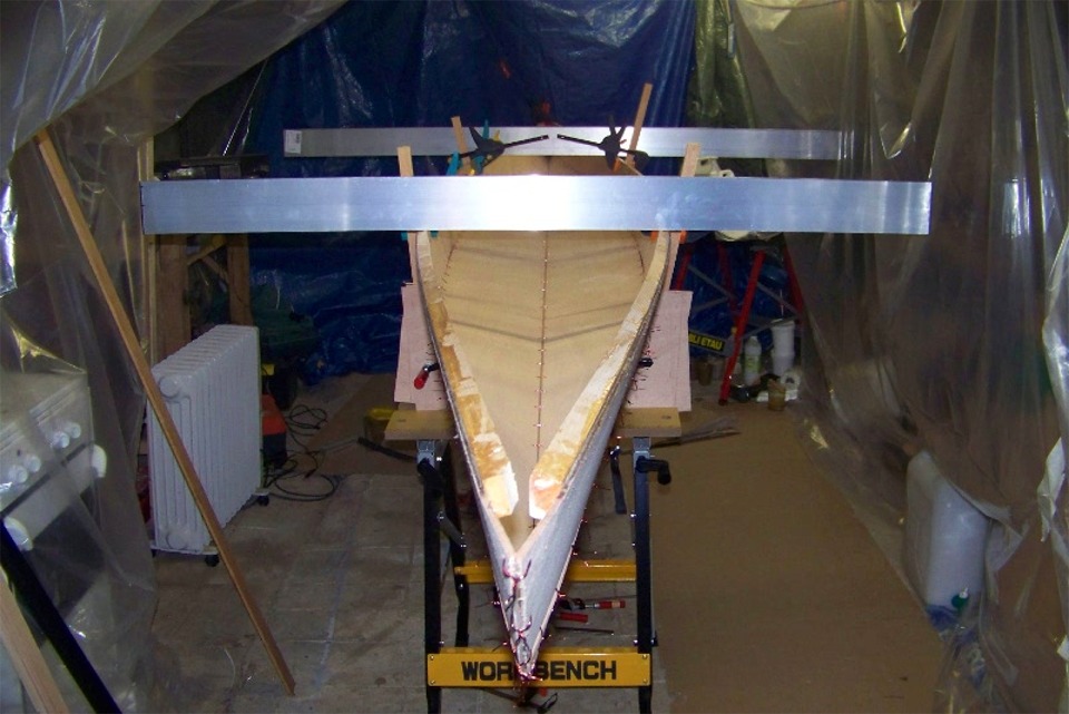 La coque cousue est retourn&eacute;e et "suspendue" afin de r&eacute;gler son orthogonalit&eacute; : la torsion &eacute;ventuelle est visualis&eacute;e gr&acirc;ce aux deux r&egrave;gles en aluminium. D&egrave;s que tout est bon, Beno&icirc;t proc&egrave;de au collage &agrave; l'&eacute;poxy. 