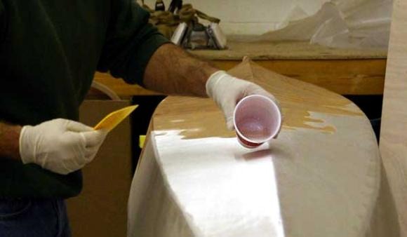 Et la résine époxy est répandue sur le tissu. Elle est répartie sur la surface à l'aide de la "squeegee", la petite raclette jaune visible dans la main droite de l'opérateur. 