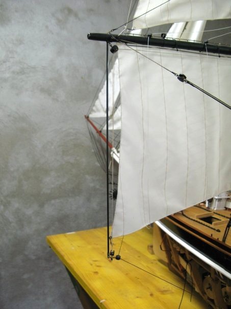 Une des rares licences prises avec l'original (à part l'aileron de 20 kg !) : le point d'écoute des voiles basses est repris sur un jonc de fibre de carbone fixé dans la vergue et permettant de l'orienter conjointement à celle-ci.