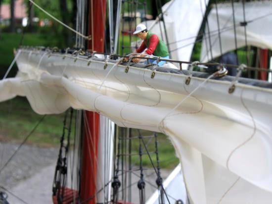 Ce gros plan sur une vergue montre la fixation des cargues, qui sont renvoyées sur des poulies situées sur la partie basse de la vergue (cachées par la voile), de là sur des poulies au collier de vergue, puis sur les treuils à fond de cale à travers les tubes de guidage en pied de mât.