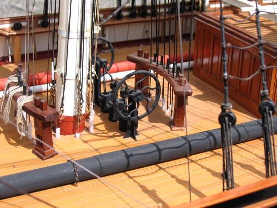 On voit également le bout des tubes de guidage autour du pied du grand mât et sous les rateliers situés devant le mât et derrière la pompe. Le cylindre noir à plat pont est une vergue de rechange, que la "grande" Cutty Sark transportait en cas de besoin.