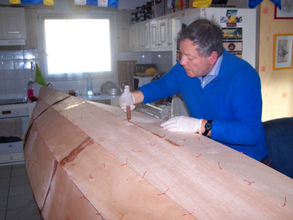 Didier en plein collage : il injecte l'&eacute;poxy charg&eacute;e dans les joints entre les panneaux de coque, pr&eacute;alablement assembl&eacute;s par des sutures en fil de cuivre. 
