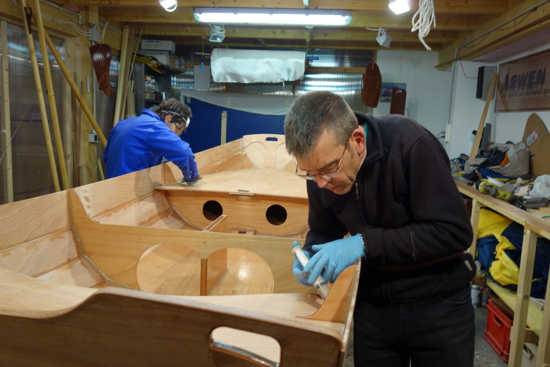 Marie-Pierre ramasse les exc&eacute;dents d'&eacute;poxy charg&eacute;e sur le cot&eacute; du joint du si&egrave;ge avant tandis que Jean d&eacute;pose l'&eacute;poxy dans l'angle &agrave; la seringue. 