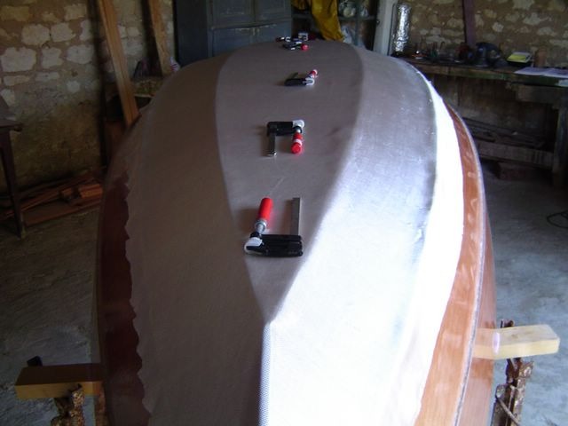 Pr&eacute;paration de la stratification : le tissu est coup&eacute; et drap&eacute; sur la coque, les presses &eacute;vitent que le tissu s'envole dans un courant d'air. Comme pour beaucoup de nos autres bateaux, seule la partie basse de la car&egrave;ne sera stratifi&eacute;e, &agrave; l'int&eacute;rieur comme &agrave; l'ext&eacute;rieur.