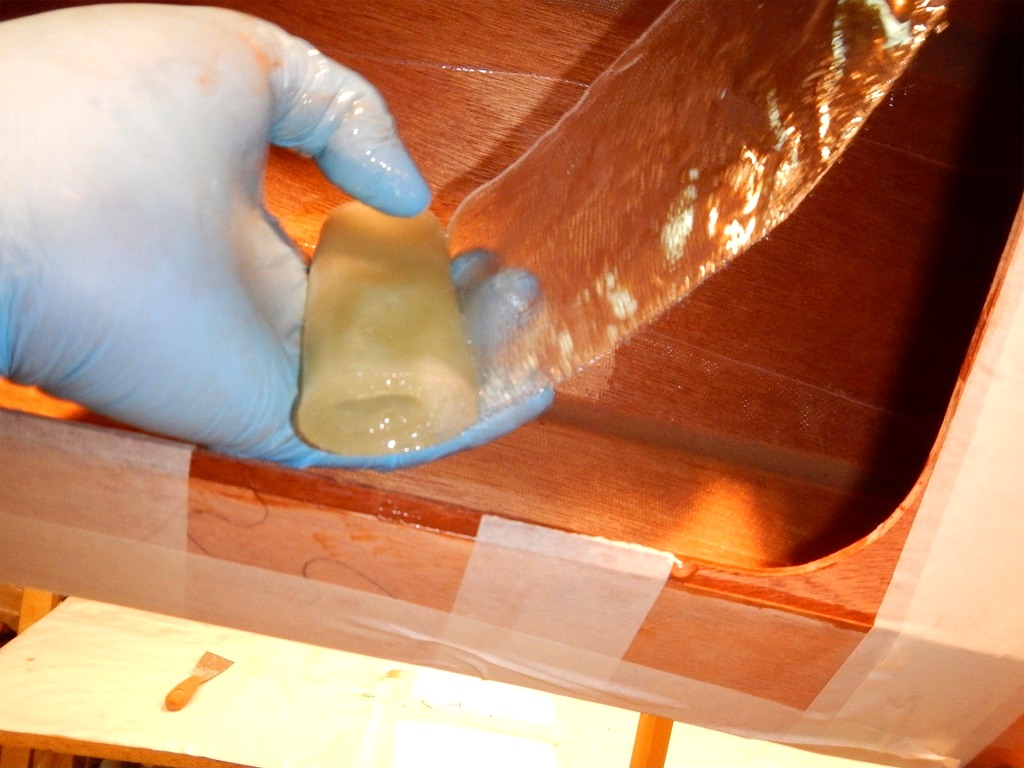 Nous déroulons partiellement les pièces de bande de fibre de verre saturée d'époxy afin de les positionner sur le joint que nous venons de faire, puis nous poussons à la main le rouleau pour le dérouler aussi loin que nous pouvons. 