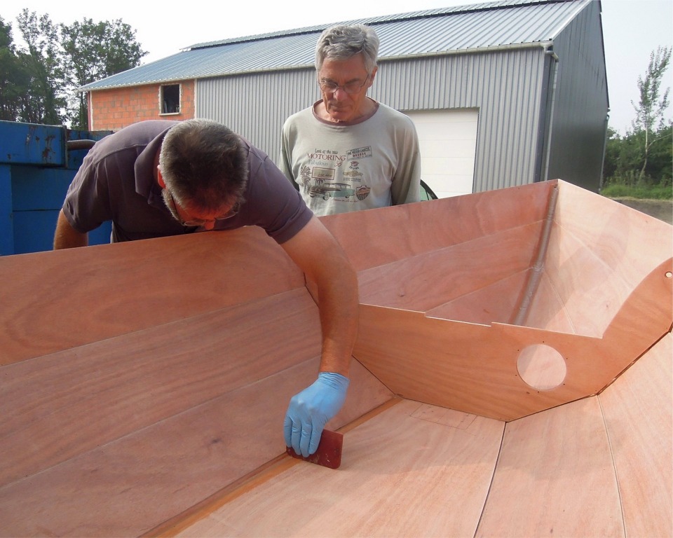 L'&eacute;poxy des collages de la veille au soir a suffisamment durci et nous remettons les coques &agrave; l'endroit pour couper toutes les sutures et d&eacute;poser la cloison centrale. Nous les retournons de nouveau afin d'extraire les sutures (&agrave; la pince et en les chauffant quand elles sont prises dans l'&eacute;poxy), puis nous commen&ccedil;ons &agrave; faire les joints sur l'int&eacute;rieur de la coque. Je montre ici comment lisser le joint entre la sole et le bord&eacute; 1 &agrave; l'aide du coin arrondi d'une squeegee.