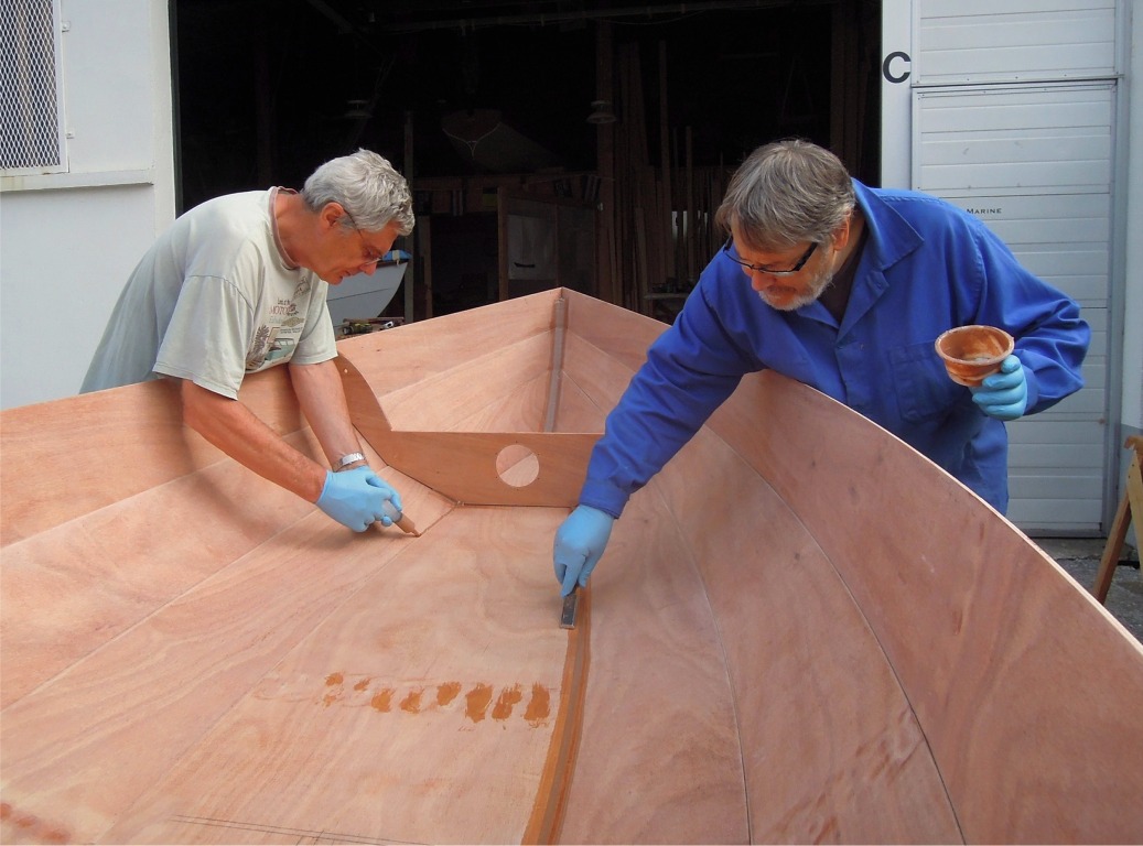 Apr&egrave;s le lissage du joint, il faut ramasser les exc&eacute;dents d'&eacute;poxy, ce que fait Jean-Fran&ccedil;ois &agrave; l'aide d'un ciseau &agrave; bois, tandis que Christian d&eacute;pose un cordon d'&eacute;poxy charg&eacute;e sur l'autre bord de la sole. Les exc&eacute;dents d'&eacute;poxy charg&eacute;e sont imm&eacute;diatement recycl&eacute;s pour faire d'autres joints. 