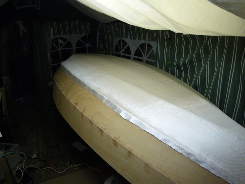 Il est maintenant temps de stratifier le fond de la coque : le tissu de verre est coupé et drapé sur le bateau. 