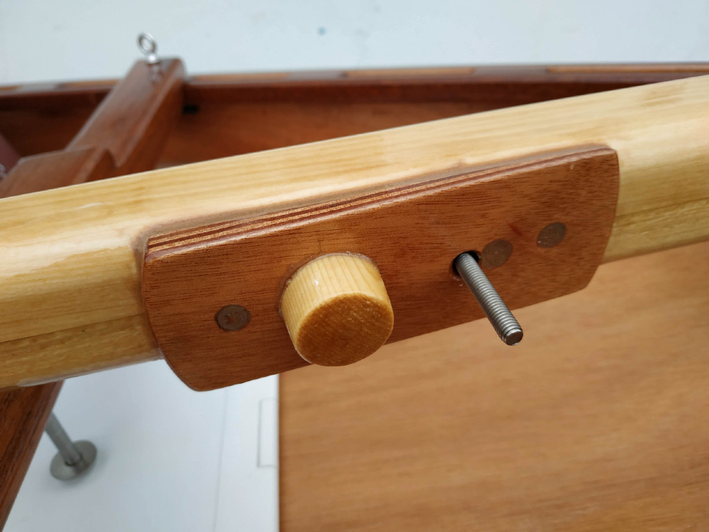 Vue du dessous de la plaque de fixation dans la guirlande. La pièce cylindrique en épicéa s'encastre dans le trou de la guirlande et le piton est tenu, lui aussi, par un écrou à oreilles. 