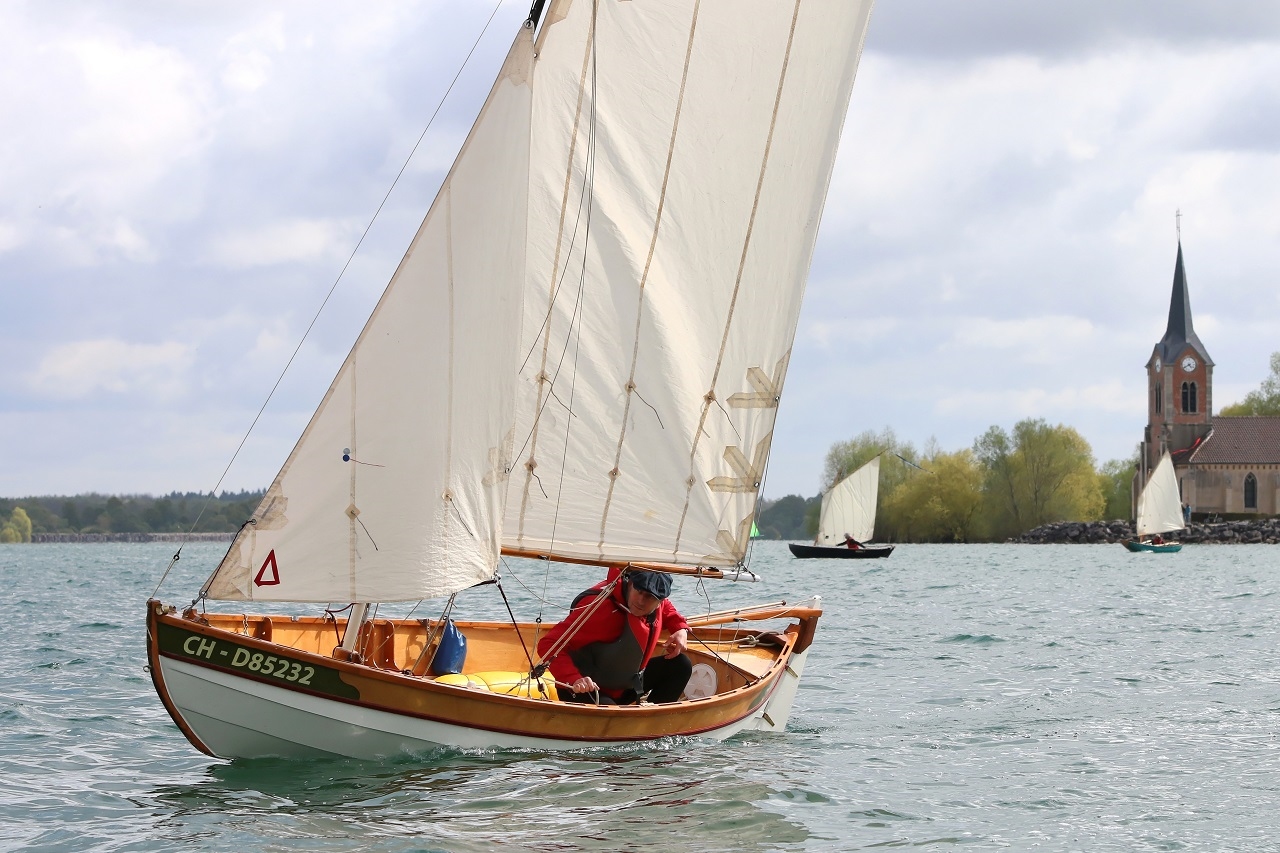 Ludo règle le foc sur "Anouket", le Skerry qu'il a construit sur plans en l'alongeant et en rehaussant le carreau, ce qui change assez significativement son aspect. On aperçoit au loin "Aldies II" et "Queen Minnie" devant l'église. 