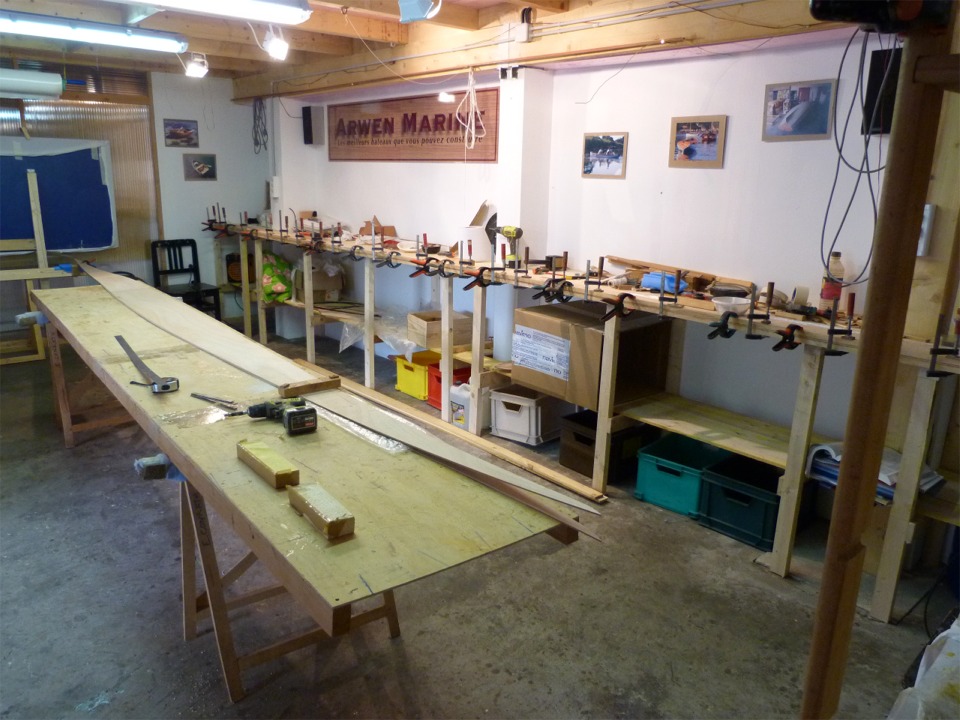 Sur la table au premier plan, je fais le collage des panneaux de fond de l'Oxford Shell : ils sont en contreplaqu&eacute; de 4 mm, 1 mm de plus que les panneaux lat&eacute;raux, sur lesquels je colle les serres, sur l'&eacute;tabli mural au fond. Les serres rigidifient les panneaux lat&eacute;raux et fournissent une surface de collage pour le pontage. J'ai eu des soucis sur le collage de ces scarfs, et j'ai du en d&eacute;coller une partie pour les recoller car ils n'&eacute;taient pas strictement align&eacute;s : sur un bateau aussi long et aussi fin, l'alignement est primordial. 