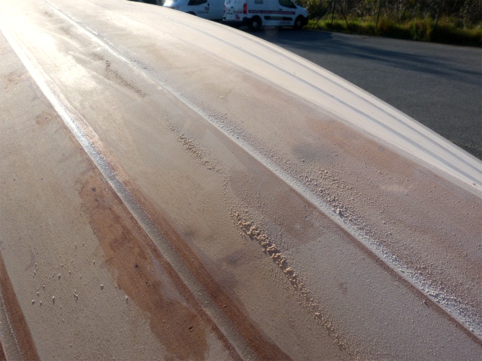 Encore un ponçage après cette deuxième couche : je suis déjà passé sur le joint de droite, mais pas encore sur celui de gauche. On voit (sur la grande version de cette image) qu'il va falloir passer une seconde couche aussi sur les trous des sutures (en bas à gauche): le contreplaqué a "bu" l'époxy chargée. Je profite aussi de ce ponçage pour arrondir très légèrement les arêtes de clins, trop aigües pour prendre l'époxy des couches d'imprégnation à venir, puis la peinture. 