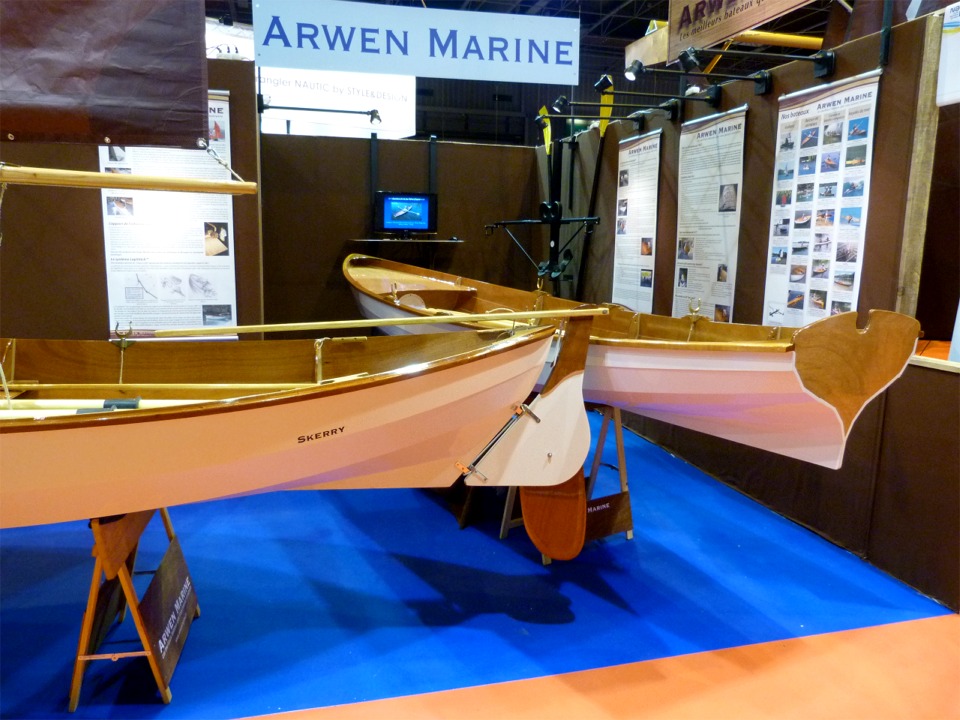 Au fond du stand, un écran d'ordinateur permet de visionner le fonds d'images du site Arwen Marine en diaporama. A droite de celui-ci, le Piantedosi Row-Wing et ses avirons carbone-verre sont accrochés à la cloison. 