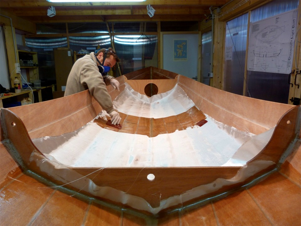 Vue depuis l'arrière : au premier plan, l'intérieur du compartiment étanche et sa petite cloison qui sera pourvue d'un nable d'équilibrage de pression dans le petit trou central. On voit que l'intérieur du caisson arrière a déja été stratifié, il ne reste plus qu'à couper l'excédent de tissu sur la cloison. Nous venons de verser 240 ml de résine au milieu de la pièce de tissu de verre disposée dans le compartiment central et, à l'aide des squeegees, nous poussons l'époxy vers l'extérieur en la faisant pénétrer pour saturer le tissu, qui devient ainsi transparent. 