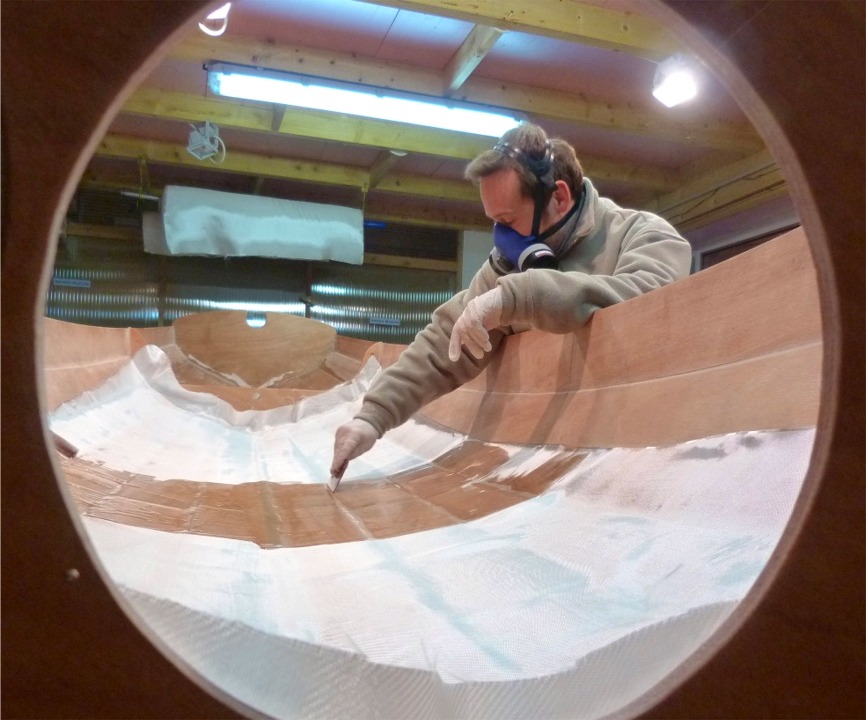 La difficult&eacute; de l'op&eacute;ration, dans la Yole de Chester, est due au passage des multiples joints entre les virures, le long desquels le tissu de verre doit suivre une courbure en "S", propice &agrave; la formation de bulles, que nous chassons sans rel&acirc;che. 