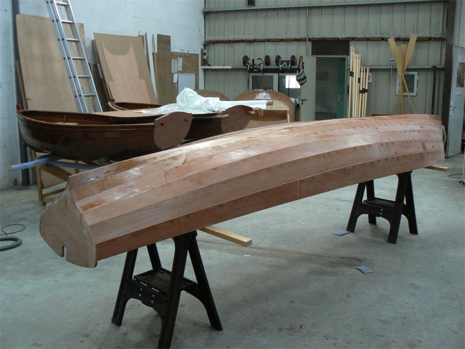 17 juillet : La yole a re&ccedil;u sa stratification ext&eacute;rieure verre/&eacute;poxy tout le long des 2 bord&eacute;s de fond, plus l'&eacute;trave et un triangle couvrant l'arri&egrave;re des 3 bord&eacute;s de fond. Une feuille de CP en travers des 2 Arwen fait table de d&eacute;coupe pour le tissu de verre