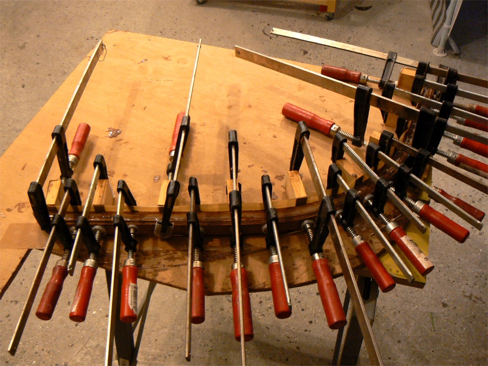 Fabrication de l'étrave extérieure en lamellé-collé. Les presses tiennent les plis de sapelli sur les taquets de la forme, eux-mêmes vissés sur une chute de contreplaqué. 