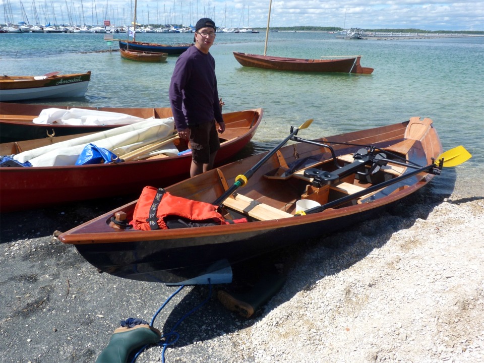 Nicolas nous fait visiter les aménagement d'Aldies II : les trois bancs sont presque standards, et Martial a ajouté des bancs latéraux (peints en bleu marine) qui joignent le banc milieu au petit siège arrière en passant par le banc arrière. L'angle de vue et le gilet de sauvetage masquent l'installation d'étambrai réversible et la flottabilité qu'il a ajoutée dans la proue. On aperçoit le puits de dérive sous le banc central et le portant. 