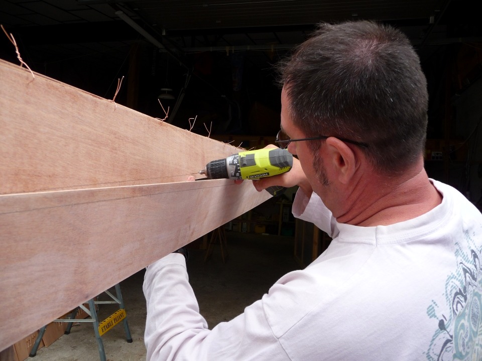 Emmanuel perce un trou de suture dans le bord haut du bordé 1, en face du trou correspondant dans le bord bas du bordé 2 (on considère haut et bas sur la coque à l'endroit, prenez votre temps pour relire, ce sera plus clair). Sur les kits les plus récents (ou récemment révisés), tous les trous des sutures sont déja percés par la machine qui fait aussi la découpe numérique. Ce n'est donc pas encore le cas de la Yole de Chester. 