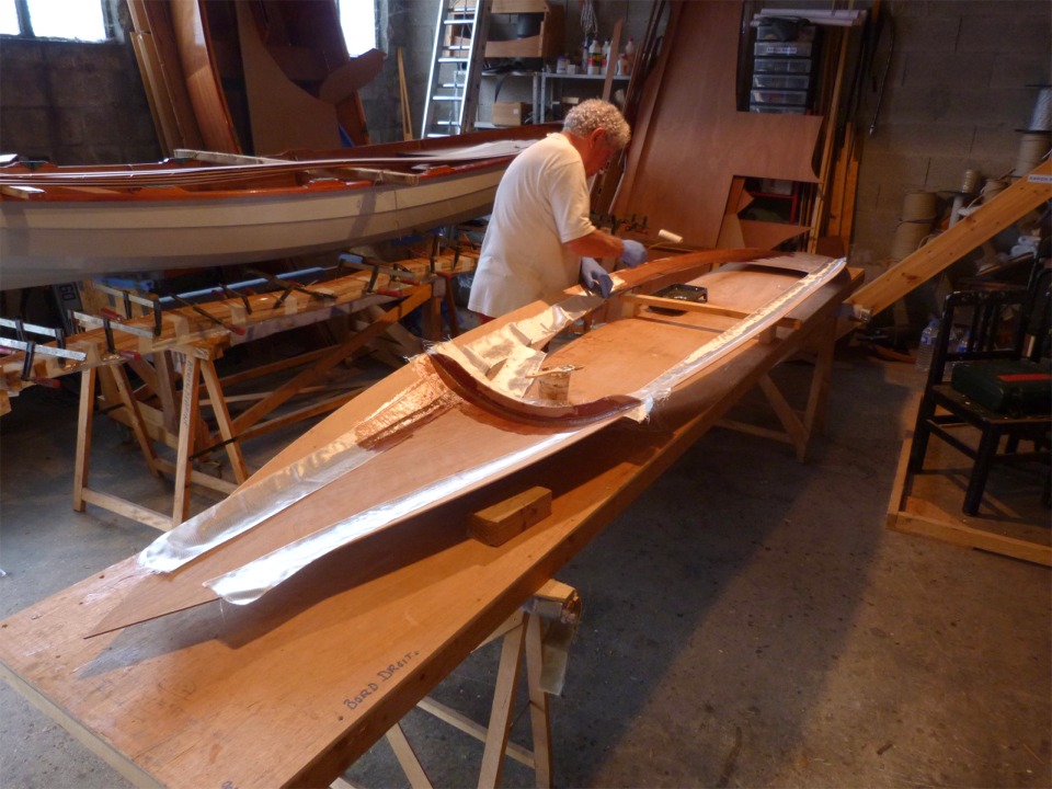 Le lendemain, 3e jour, Pierre est occup&eacute; &agrave; saturer d'&eacute;poxy les bandes de fibre de verre qui renforcent tous les joints sous le pontage (le dessus sera stratifi&eacute; avec un tissu de verre l&eacute;ger sur toute sa surface apr&egrave;s collage du pontage sur la coque). 