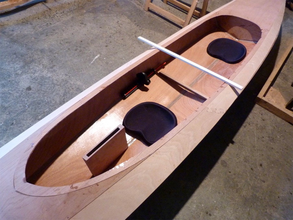 Nous avons pos&eacute; le Wood Duck Double au sol et dispos&eacute; les si&egrave;ges, les cale-pieds arri&egrave;re, le puits de d&eacute;rive et un tasseau &agrave; l'endroit o&ugrave; le bras de liaison arri&egrave;re traverserait le cockpit. Pierre s'est install&eacute; dans le kayak afin d'ajuster cet am&eacute;nagement. Nous avons envisag&eacute; de d&eacute;placer le bras arri&egrave;re, mais la cloison de renfort que nous allons coller dessous (mat&eacute;rialis&eacute;e par le petit tasseau au fond du kayak) limite les options possibles, &agrave; cause notamment de l'interaction avec les cales-pieds. 