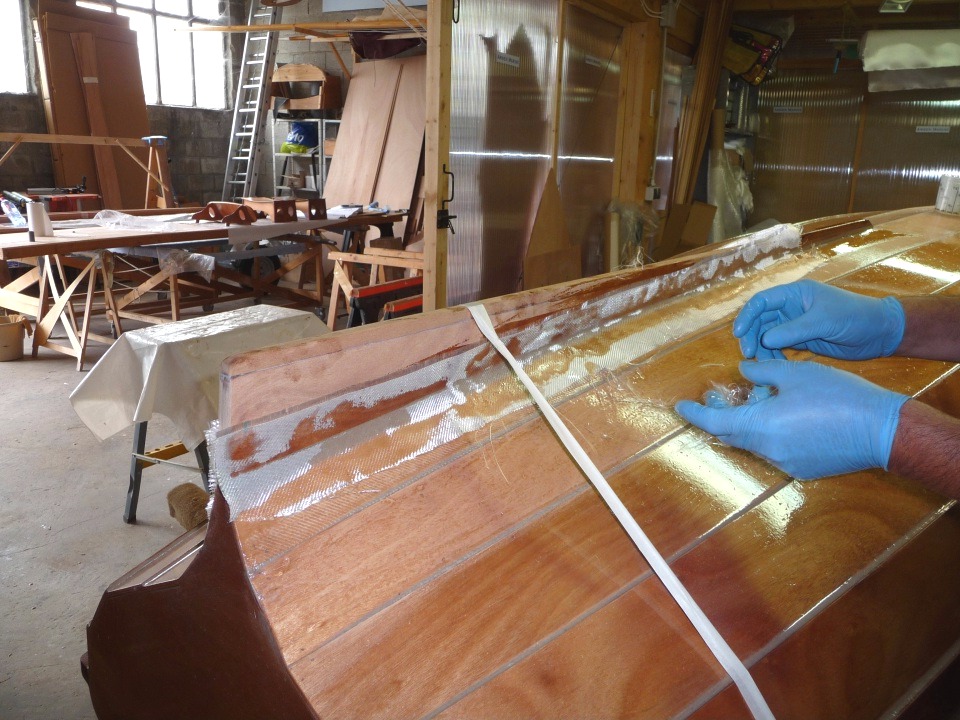 Voici la bande coté bâbord en place. Le tissu de verre est partiellement "mouillé" par la résine que j'ai appliquée préalablement, et je vais maintenant terminer de la saturer, après avoir jeté les fibres que j'ai dans les mains.