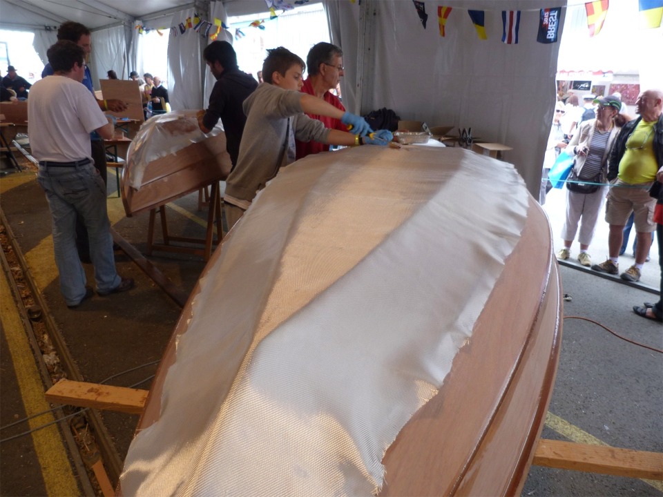 Nous avons drapé le tissu sur la coque et découpé en dépassant de 5 cm la zone à stratifier, identique à celle que nous avons réalisée sur l'intérieur : la sole et les deux bordés 1. Ainsi, toute la partie basse du bateau est prise en sandwich par la stratification intérieure et extérieure, ce qui le renforce et le rigidifie considérablement. 