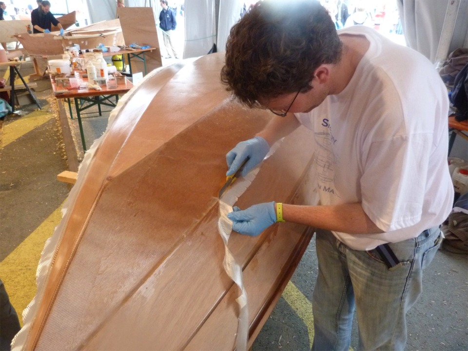 Erwan coupe l'excédent de tissu de verre au cutter en appuyant la lame sur le joint d'époxy, qui ne "marquera" pas pendant la découpe, contrairement à la surface du contreplaqué. 