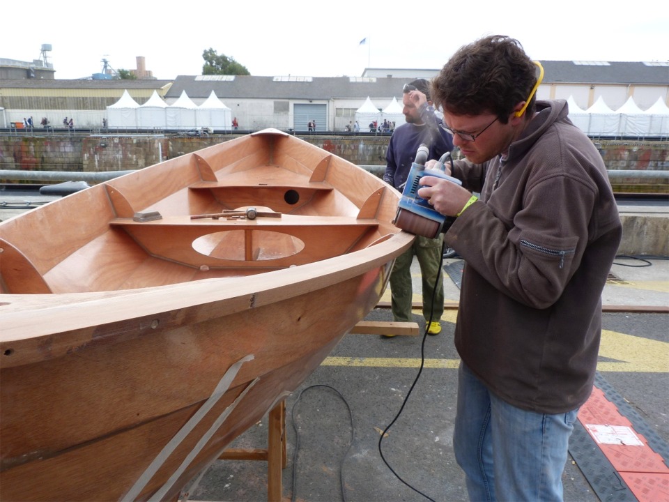 Dernière journée !!! Nous sortons les Skerry à l'extérieur du chapiteau "Je construis mon bateau" car nous allons finir les listons à la ponceuse à bande et à la défonceuse. Nous allons donc faire beaucoup de poussière qui rendrait l'air irrespirable à l'intérieur (d'autant plus que la poussière de bois rouge est particulièrement nocive pour les poumons). 