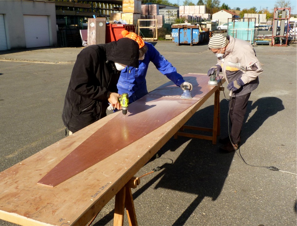 Nous attaquons par un pon&ccedil;age g&eacute;n&eacute;ral des &eacute;l&eacute;ments du kit, tout en reper&ccedil;ant les trous des sutures, maintenant pr&eacute;perc&eacute;s pour ce kit, ce qui est un grand confort, car on n'a plus &agrave; se pr&eacute;occuper de positionner ces trous. Cyrille est &agrave; la perceuse, Marie-Pierre et Jean aux ponceuses orbitales. Denis arondit les ar&ecirc;tes des membrures hors du cadre. 