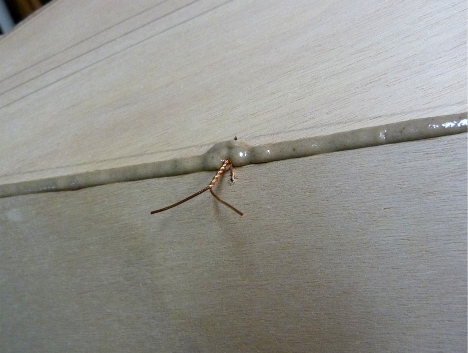 Gros plan sur une des sutures entre la sole et le bordé 1 sur l'arrière à bâbord. Les traits que l'on aperçoit en haut à gauche de l'image sont les repères de montage pour l'aileron. Les sutures sont toutes plus ou moins noyées dans l'époxy chargée, comme celle-ci, mais on les libère facilement pour les extraire en les chauffant quelques secondes au décapeur thermique. 