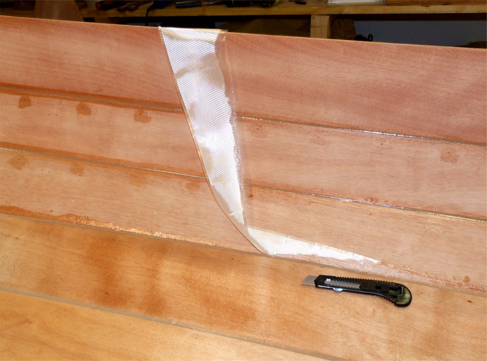 Je coupe la fibre de verre avec un cutter (lame neuve, car la fibre est un peu d&eacute;licate &agrave; couper) en m'appuyant sur le joint d'&eacute;poxy entre les bord&eacute;s 1 et 2. En effet, pas question de couper sur le contreplaqu&eacute; car la pointe de la lame ferait une marque permanente. 