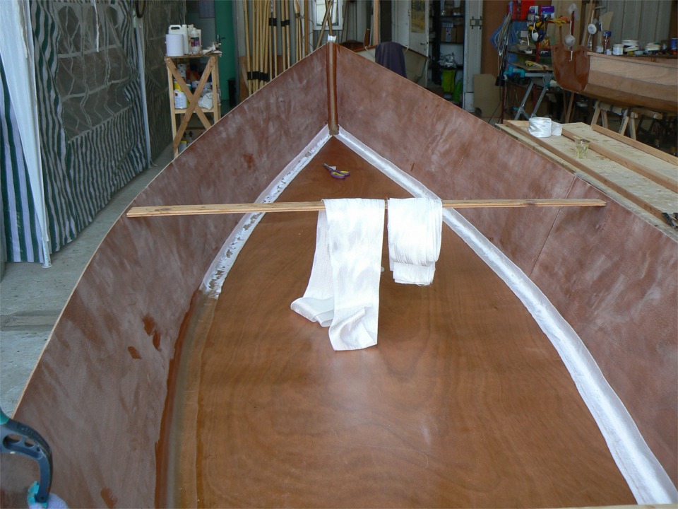 Sur cette image, je suis en train d'imprégner la première épaisseur de tissu par-dessus les joints-congés. On voit que le tissu ne s'imprègne que partiellement de la résine du joint-congé, et j'ajoute de l'époxy "claire" au pinceau. Seule la première couche de tissu est en place, la seconde, plus large est en attente sur le "raidisseur". 