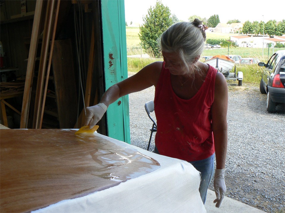 Mon épouse est venue s'initier au maniement de la "squeegee", ou raclette en français. On verse l'époxy au milieu de la zone à stratifier, et on l'étale à la raclette jusqu'à ce que le tissu soit uniformément transparent et que la trame apparaisse. Dehors, la Yole de Chester est chargée sur la remorque et prête à partir à Plouer-sur-Rance. 