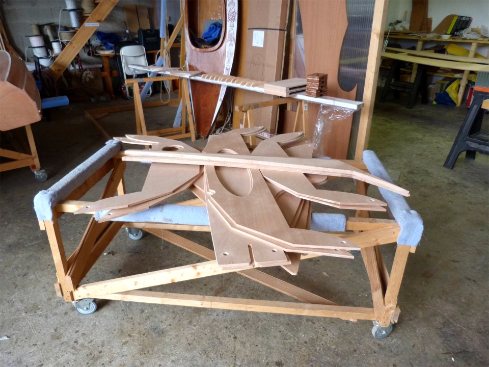 Voici une partie des pi&egrave;ces des deux kits : au premier plan sur le chariot, toutes les cloisons et les si&egrave;ges, sous les deux ailerons coll&eacute;s et munis de leur semelle. Les bords expos&eacute;s sont arrondis, les trous son faits On aper&ccedil;oit &agrave; l'arri&egrave;re-plan les 4 guirlandes, les 12 cale-pieds, les deux puits de d&eacute;rive et les 5 pieds de m&acirc;t (l&agrave; j'ai pris un peu d'avance)... 