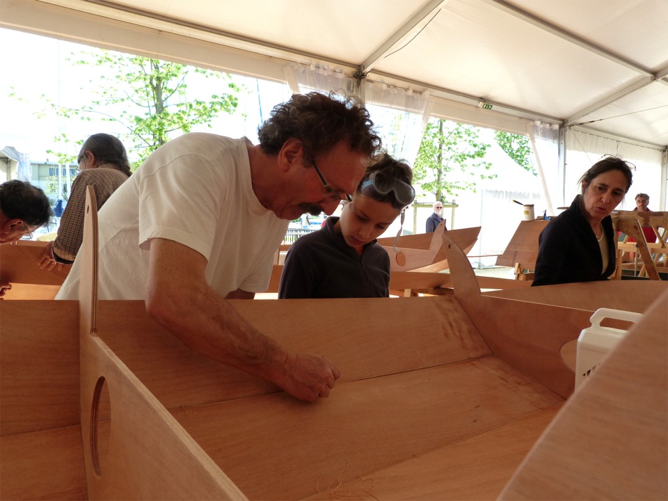 Robert montre à Vincent comment passer et nouer une suture de fil de cuivre sous l'oeil de Caroline qui immobilise le bordé 2 tribord en cours de couture. 