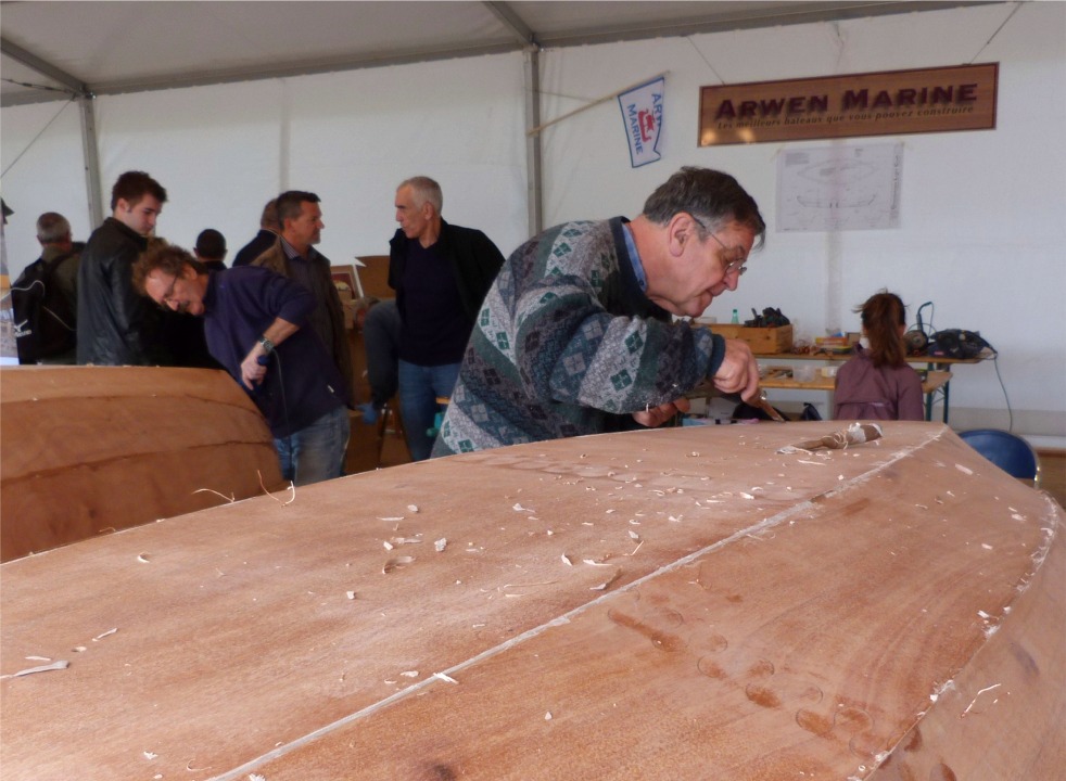 Le travail sur l'intérieur est essentiellement terminé, il ne reste plus qu'à passer une couche d'époxy claire sur les bordés et les sièges. Nous avons donc enlevé les presses qui tenaient le premier pli des listons pendant leur collage; puis nous avons retourné les deux coques afin de finir le travail sur la surface extérieure. Nous commençons par gratter les gros excédents d'époxy chargée, notamment les "vagues" causés par les sutures (rappelle toi, Barbara...) 