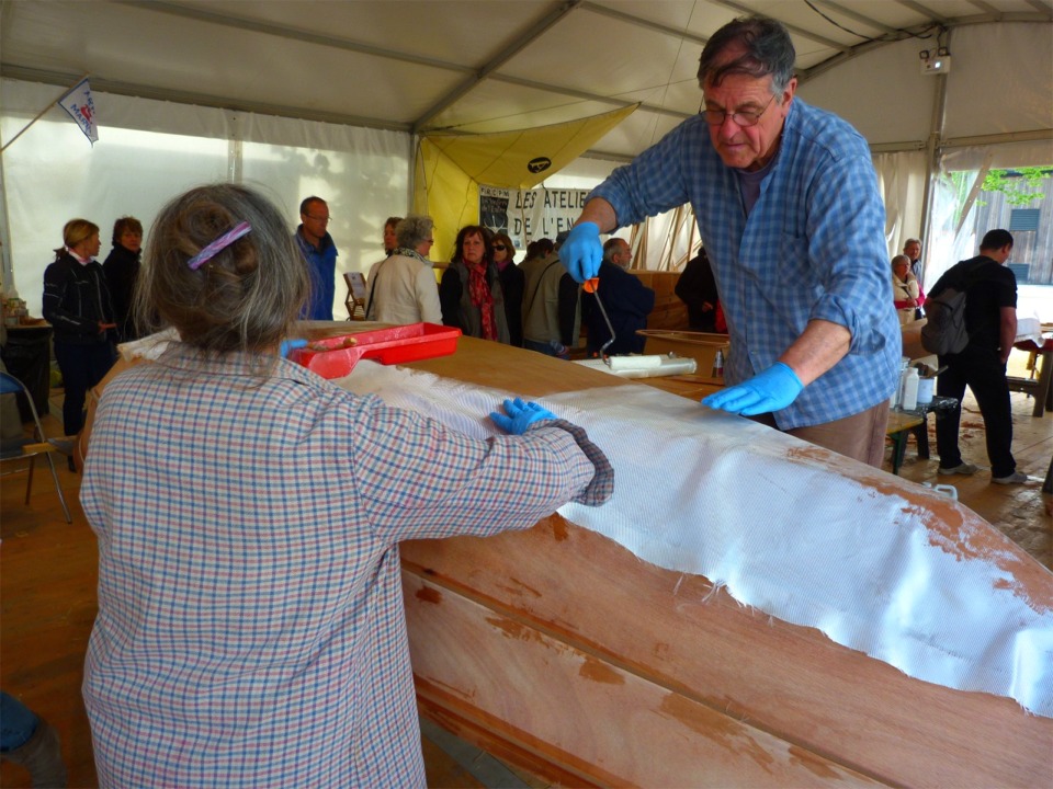 La pièce principale de tissu de verre est rabattue en place et saturée de résine à son tour. Nous utilisons des rouleaux pour cette opération. Notez que la fibre s'est déja partiellement "mouillée" d'époxy par capillarité aux endroits des bandes de fibre de renfort. 
