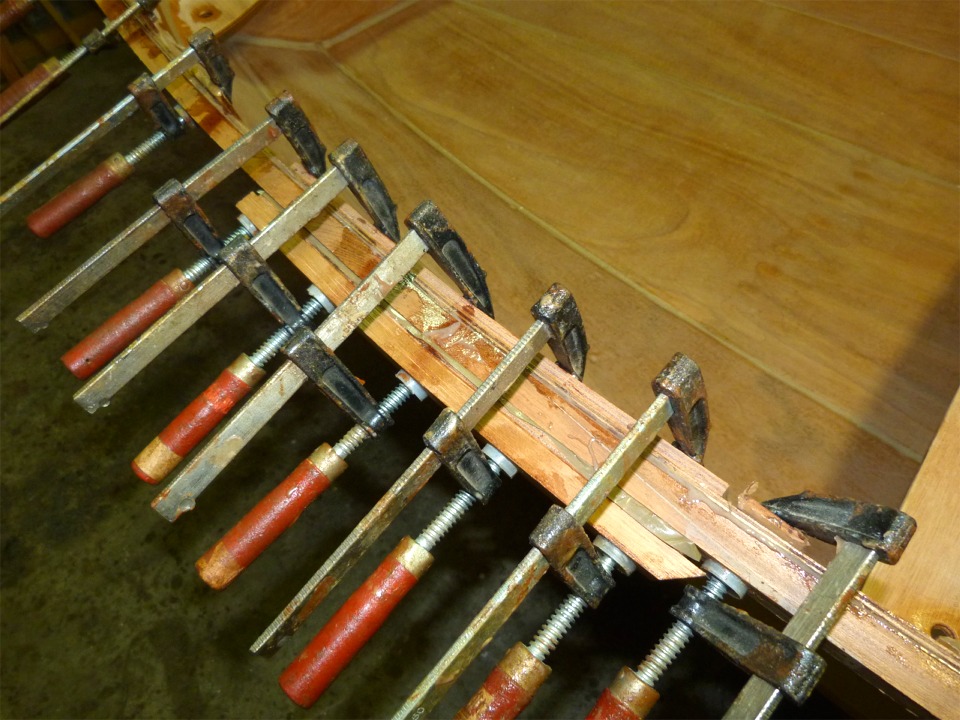 Lorsque la latte a cass&eacute;, j'avais deux options : tout d&eacute;monter, recouper et coller un scarf sur la latte cass&eacute;e et recommencer deux jours plus tard ou bien continuer en fixant une atelle. C'est cette seconde solution que j'ai choisie, comme on le voit sur l'image. Il faut dire que la temp&eacute;rature rendait l'option 1 hasardeuse car l'&eacute;poxy commen&ccedil;ait d&eacute;ja &agrave; prendre. J'ai donc align&eacute; du mieux possible les deux bouts de la cassure, pos&eacute; cette attelle (compos&eacute;e de deux lattes de CP makor&eacute; miraculeusement disponibles &agrave; la bonne taille et "rang&eacute;es" &agrave; proximit&eacute; et d'une chute de liston h&eacute;rit&eacute;e d'un Skerry ant&eacute;rieur) et cogn&eacute; au marteau sur le bout de la latte pour fermer au maximum la cassure. 