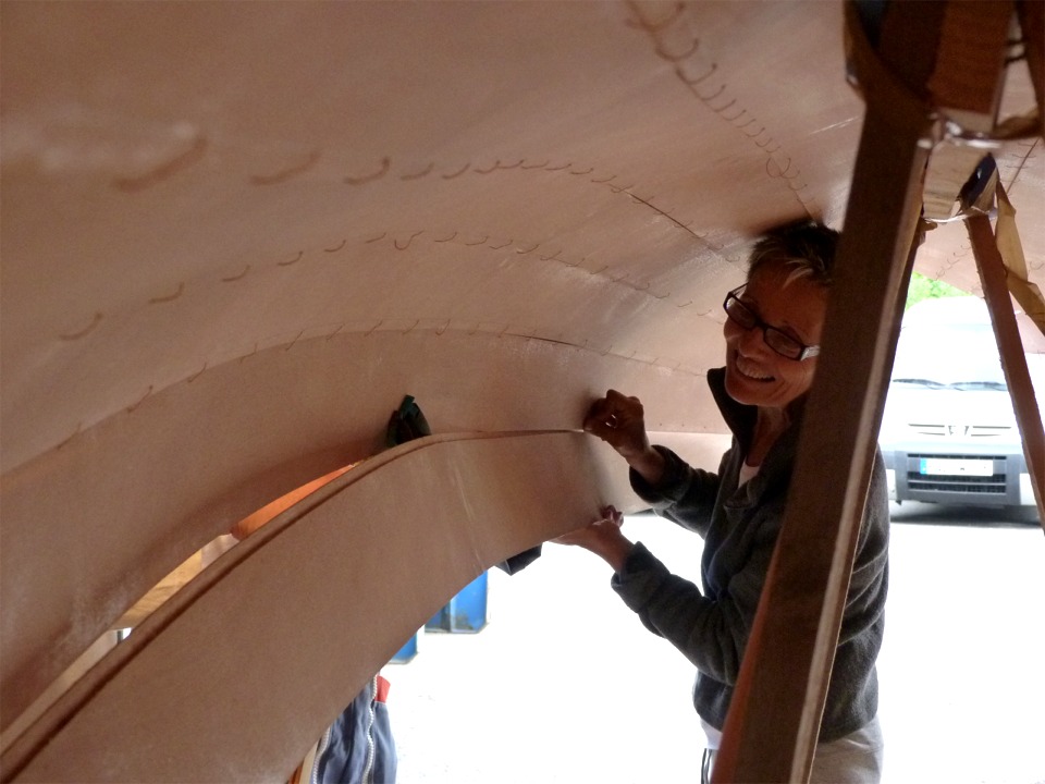 Annick s'est gliss&eacute;e sous la coque afin de passer les sutures plus facilement. On aper&ccedil;oit devant elle la pince qui tient la b&eacute;quille b&acirc;bord. Les sutures sont pli&eacute;es en "U" et pass&eacute;es de l'int&eacute;rieur vers l'ext&eacute;rieur. 