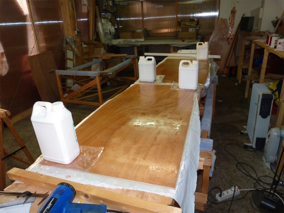 En parall&egrave;le, je stratifie un tissu de verre sur les panneaux des dessus des ballasts. Les bidons plac&eacute;s transversalement servent &agrave; contrer le voilage de ces panneaux. J'esp&egrave;re qu'une fois la stratification durcie, ils conserveront leur plan&eacute;it&eacute; forc&eacute;e. Cette d&eacute;formation de certaines pi&egrave;ces peut provenir de la fabrication ou du stockage des feuilles de contreplaqu&eacute;, heureusement c'est assez rare. 