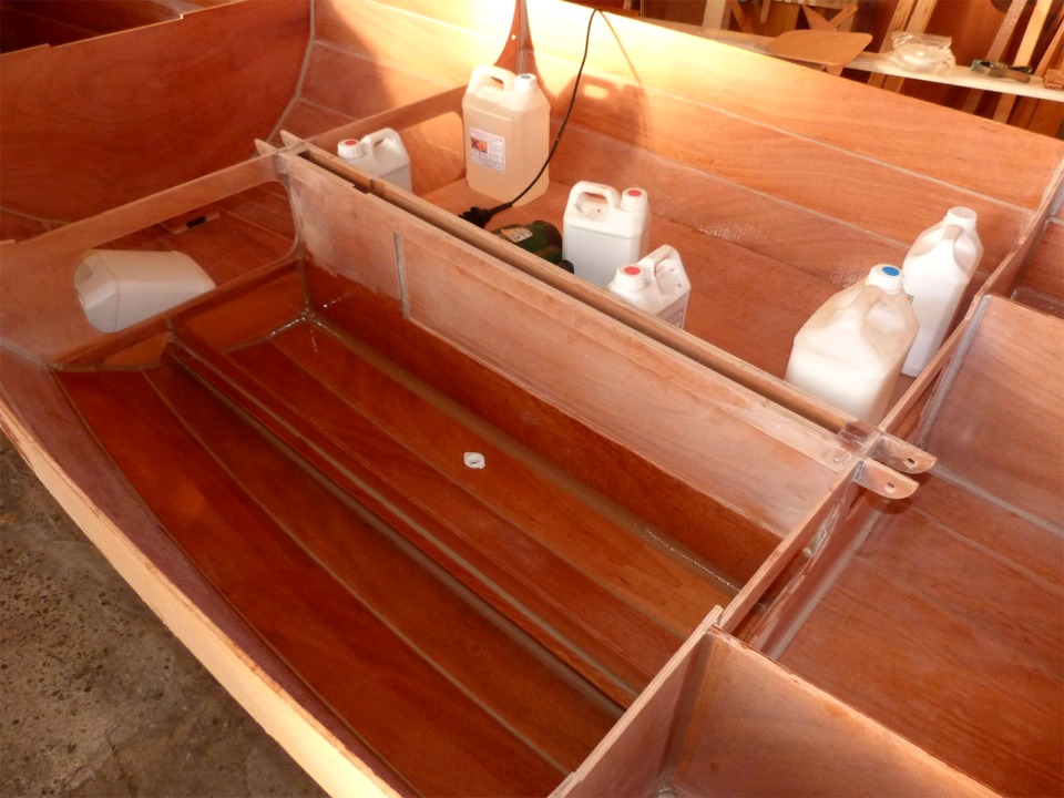 Je viens de passer une derni&egrave;re couche d'&eacute;poxy claire sur toute la surface int&eacute;rieure du r&eacute;servoir de ballast tribord, ainsi que sur la face inf&eacute;rieure du panneau de fermeture et viens de le coller. J'utilise tous ces bidons pour le presser en place &agrave; cause du voilage r&eacute;siduel qui g&ecirc;ne pour le coller uniform&eacute;ment. Au premier plan, je viens de passer la couche d'&eacute;poxy claire sur le compartiment b&acirc;bord, au fond duquel on aper&ccedil;oit le nable, coll&eacute; juste avant. Je vais maintenant appliquer un filet d'&eacute;poxy charg&eacute;e sur tout le pourtour de contact du panneau avant de le mettre en place. 