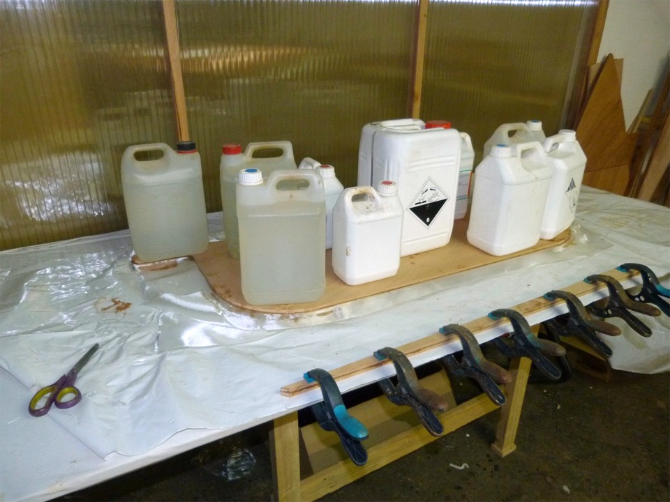 En parall&egrave;le, je colle les trois &eacute;paisseurs de contreplaqu&eacute; de 9 mm qui vous constituer la d&eacute;rive. J'ai intercal&eacute; deux &eacute;paisseurs de tissu de verre entre les couches de bois afin de rigidier et renforcer cette d&eacute;rive. J'ai stratifi&eacute; le tissu sur la face int&eacute;rieure des deux &eacute;paisseurs de contreplaqu&eacute; de l'ext&eacute;rieur avant de r&eacute;-encoller &agrave; l'&eacute;poxy l&eacute;g&egrave;rement charg&eacute;e. Le pressage est assur&eacute; par les bidons. Au premier plan, ce sont les deux &eacute;paisseurs du petit aileron qui sera coll&eacute; sous "l'aileron-caisse".