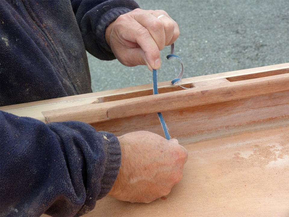 J'avais arrondi les deux ar&ecirc;tes de la serre qui sont orient&eacute;es vers l'int&eacute;rieur du bateau avant de les coller, mais les deux ar&ecirc;tes qui sont vers le bord&eacute; sont encore &agrave; angle droit et je dois maintenant arrondir les ar&ecirc;tes sur tous les "vides" entre les cales. J'utilise un bout de bande abrasive hors d'usage pour d&eacute;marrer ce travail. Je me redis que c'&eacute;tait une bonne id&eacute;e de mettre ces serres sur cales... 