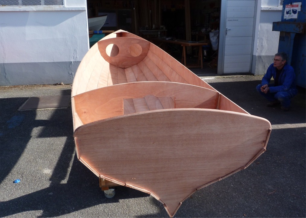 La semaine derni&egrave;re, nous avions juste fait le collage de la Yole de Chester que nous venions de coudre avec Pierre, Katia et Mattias. Ce lundi, nous poursuivons la construction accompagn&eacute;e avec Pierre, que l'on aper&ccedil;oit accroupi &agrave; droite, contemplant notre oeuvre commune et rassemblant son &eacute;nergie pour une nouvelle journ&eacute;e de travail... Nous profitons du soleil pour sortir la yole afin de poncer les joints-cong&eacute;s int&eacute;rieurs.