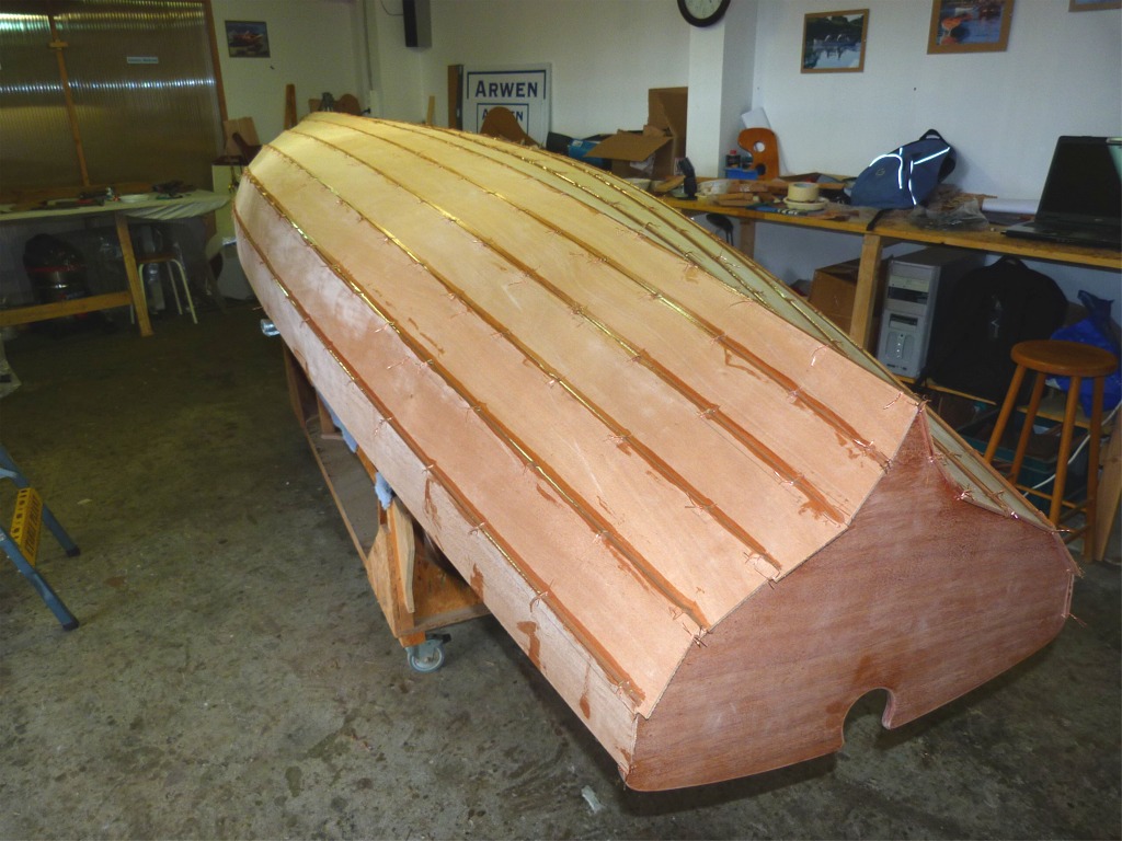 Apr&egrave;s m'avoir aid&eacute; &agrave; d&eacute;terminer l'emplacement de la structure, puis &agrave; coudre celle-ci en place, Pierre m'aide &agrave; remettre la yole &agrave; l'envers (second retournement) et &agrave; faire le premier collage &agrave; l'&eacute;poxy charg&eacute;e. Nous d&eacute;posons un filet de r&eacute;sine tout le long de chacun des joints entre les virures, puis nous lissons l'&eacute;poxy &agrave; la cuiller (afin de la pousser au fond des joints) et ramassons le plus gros des exc&eacute;dents.