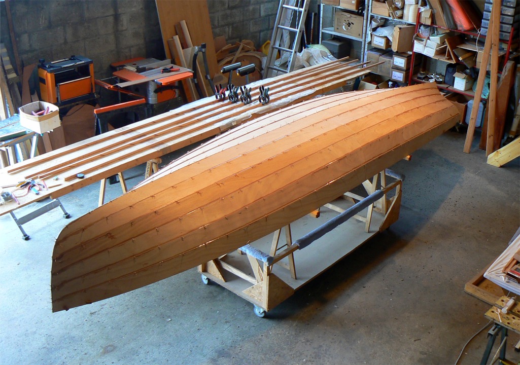 On aper&ccedil;oit sur la table derri&egrave;re la yole les listons dont les scarfs sont en cours de collage. Pour faciliter leur cintrage, chacun des listons est coll&eacute; en deux &eacute;paisseurs. 