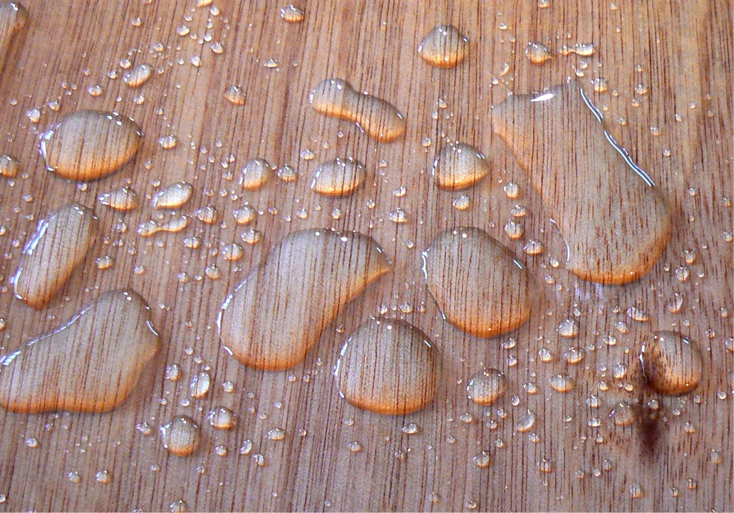 Gros plan sur les gouttes d'eau &agrave; la surface de l'okoum&eacute; verni. L'int&eacute;r&ecirc;t principal du contreplaqu&eacute; marine r&eacute;alis&eacute; &agrave; partir de ce bois pour la construction de petits bateaux est son faible poids, en plus de ses propri&eacute;t&eacute;s m&eacute;caniques correctes, sa relativement bonne r&eacute;sistance aux parasites li&eacute;s au milieu humide et son tr&egrave;s bel aspect sous le vernis. 